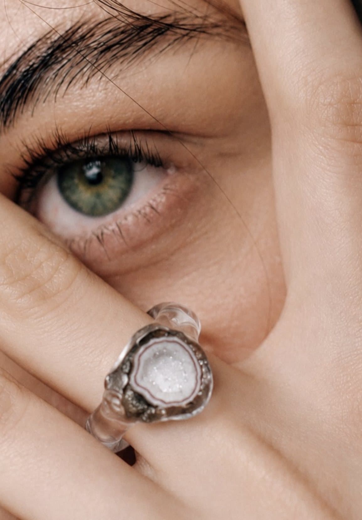 Un ojo verde detrás de una mano con un anillo de vidrio de Sosil