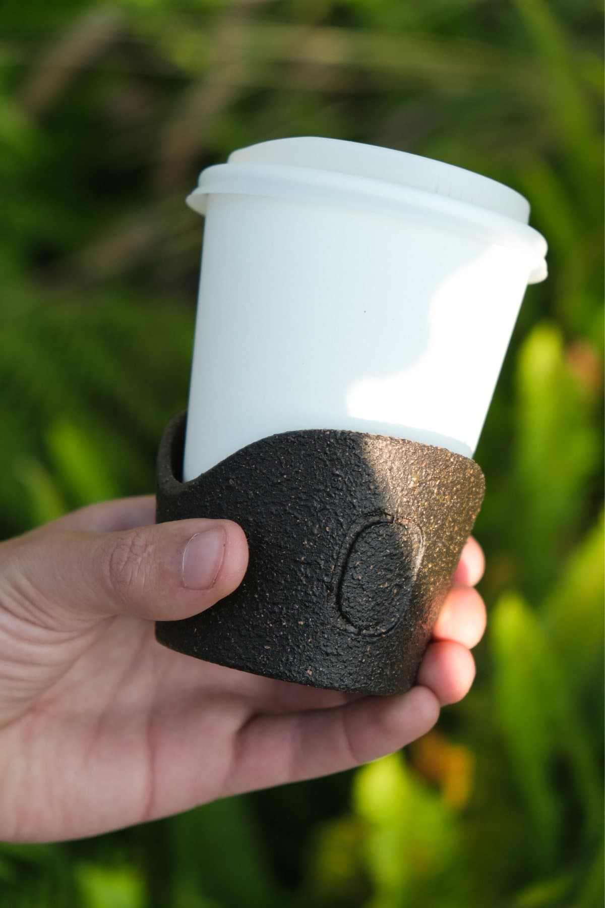 Una mano sostiene un vaso para café con funda de Terrazo
