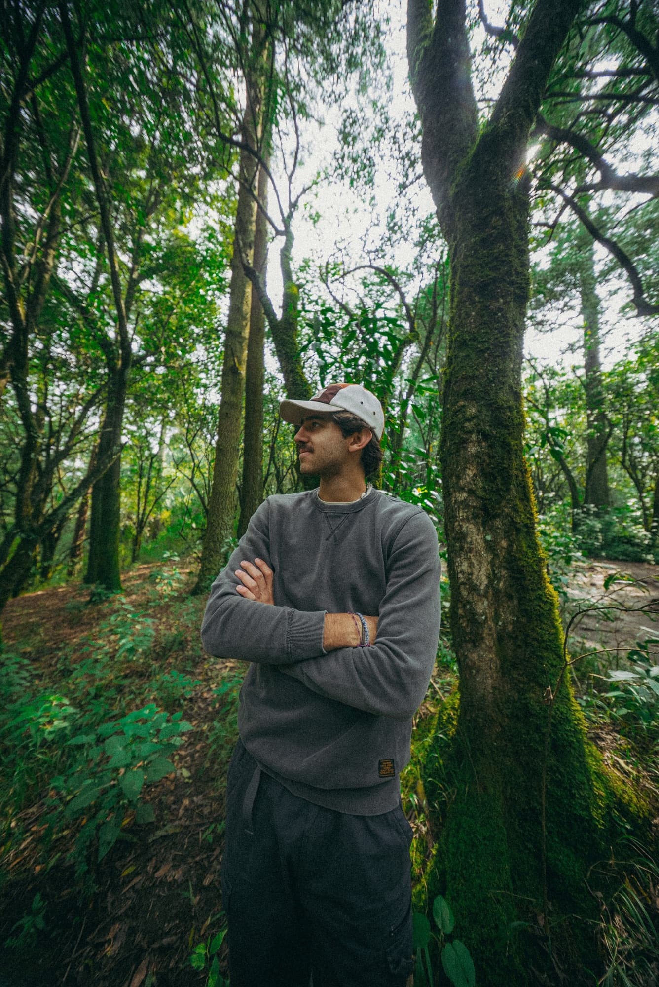 Alguien de cuerpo entero entre árboles con musgo, con la gorra puesta